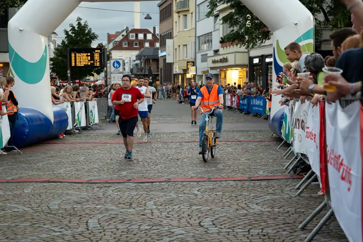 Läufer und Radfahrer beim Stadtlauf Bergisch Gladbach. Zuschauer jubeln am Streckenrand.