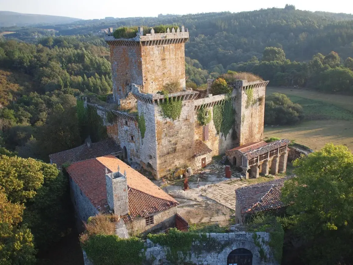 El **castillo de Pambre**, una fortaleza de piedra antigua, se alza entre bosques frondosos. Sus muros cubiertos de hiedra y tejados rojizos evocan historias de antaño.