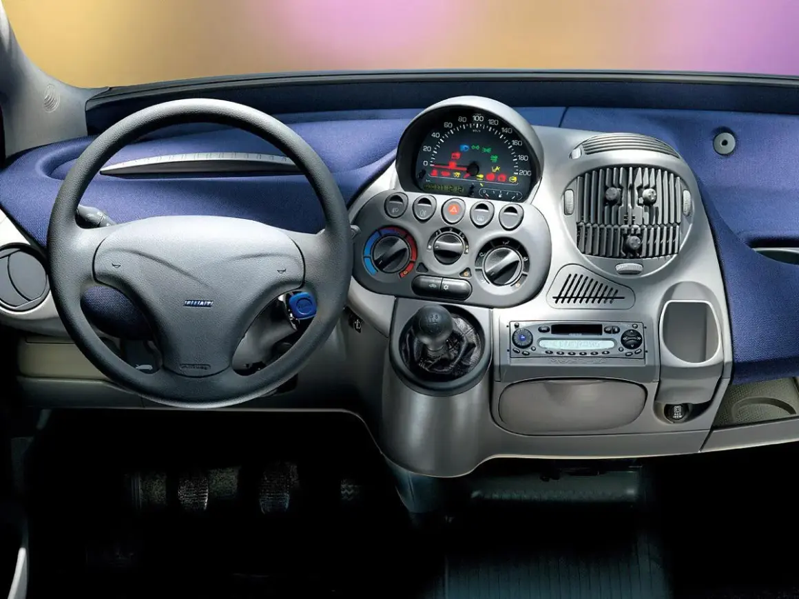 Widok na **fiat multipla wnętrze**: kierownica, deska rozdzielcza z radiem i nawiewami, dźwignia zmiany biegów.