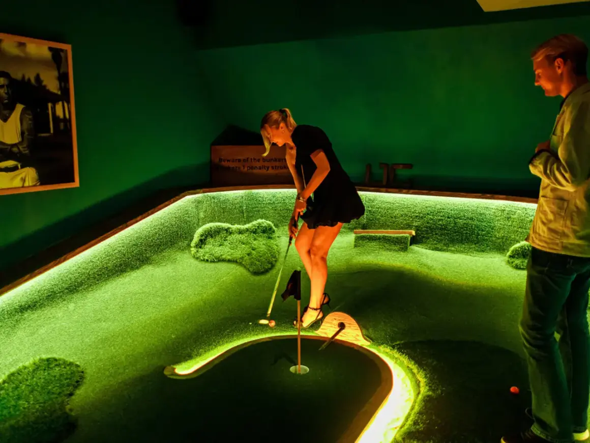 En kvinna spelar minigolf på en bana i Slottskogen. En man tittar på.