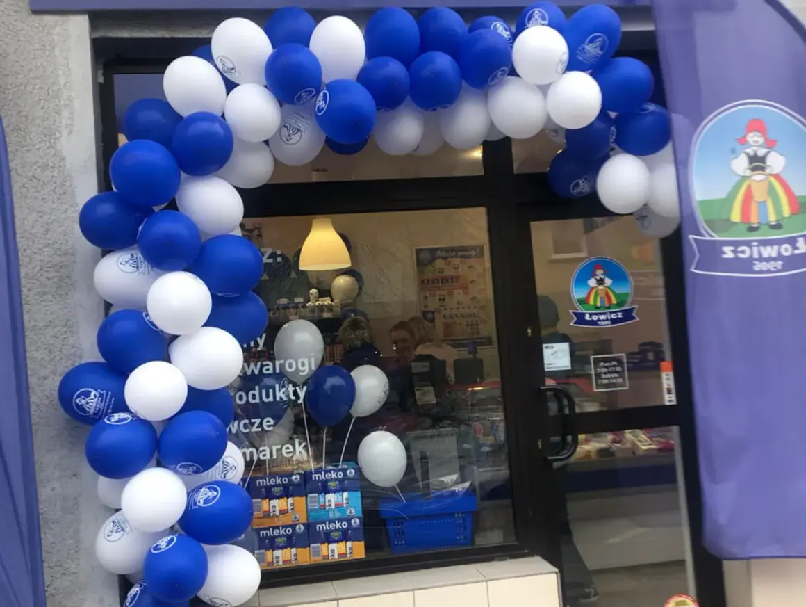 Biało-niebieskie balony tworzą łuk nad wejściem do sklepu z logo Łowicz.
