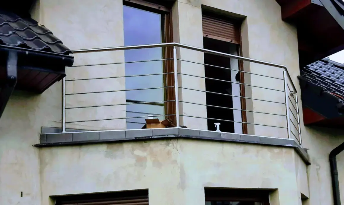 Nowoczesna poręcz ze stali nierdzewnej na balkonie, z widokiem na okna i dachówki.