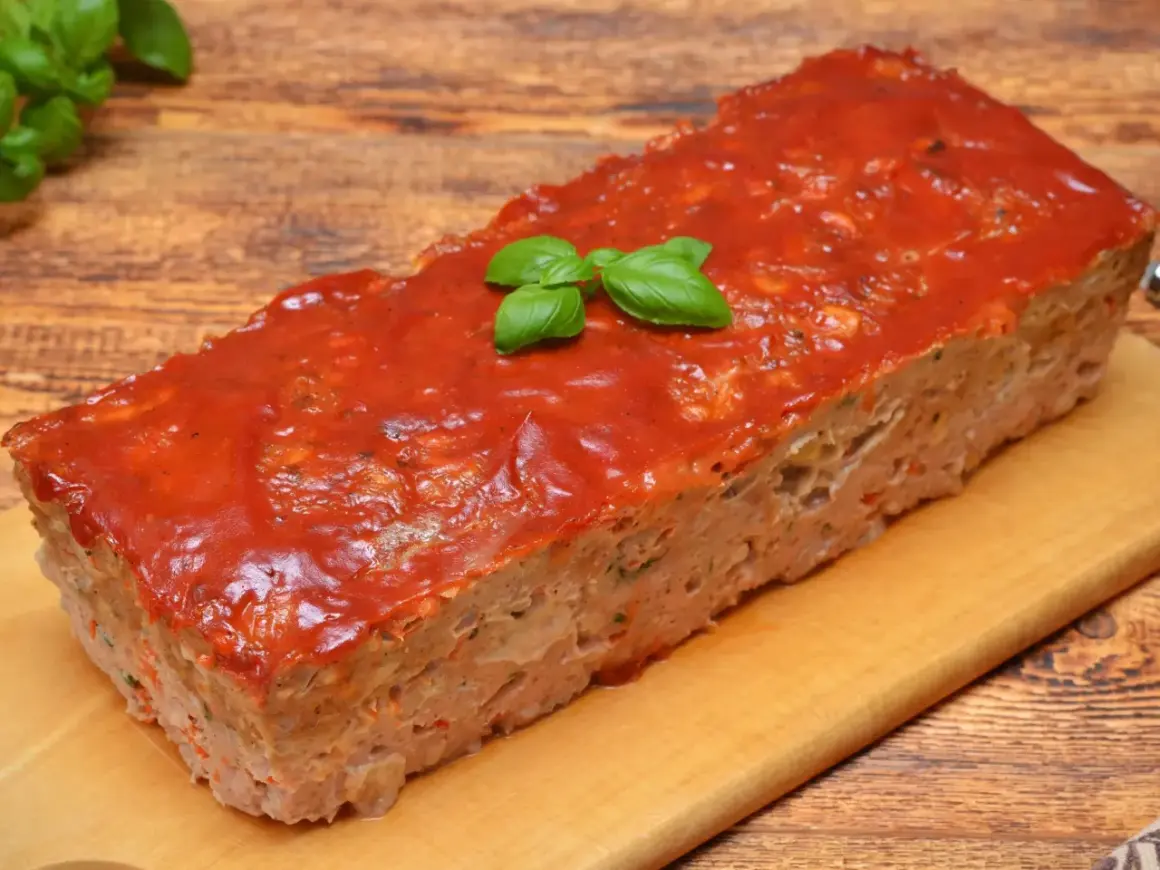 Pyszna pieczeń z mięsa mielonego na kanapki, polana sosem pomidorowym i ozdobiona listkami bazylii. Idealna na rodzinny obiad lub jako dodatek do kanapek.