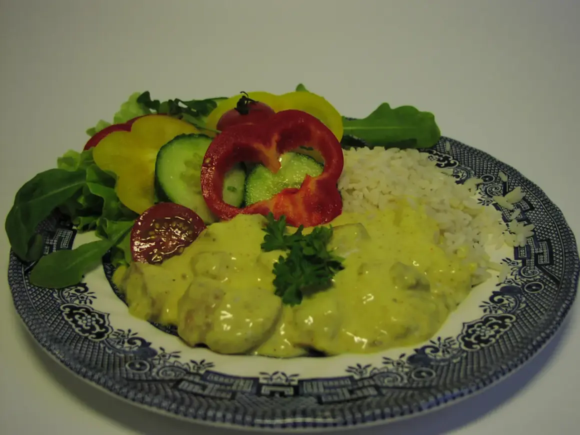 En tallrik med kyckling curry, ris och en sallad av paprika, gurka och tomat.