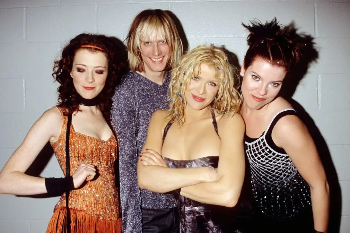 Il gruppo musicale Hole posa sorridendo. Courtney Love al centro, con i capelli biondi e un vestito scuro.