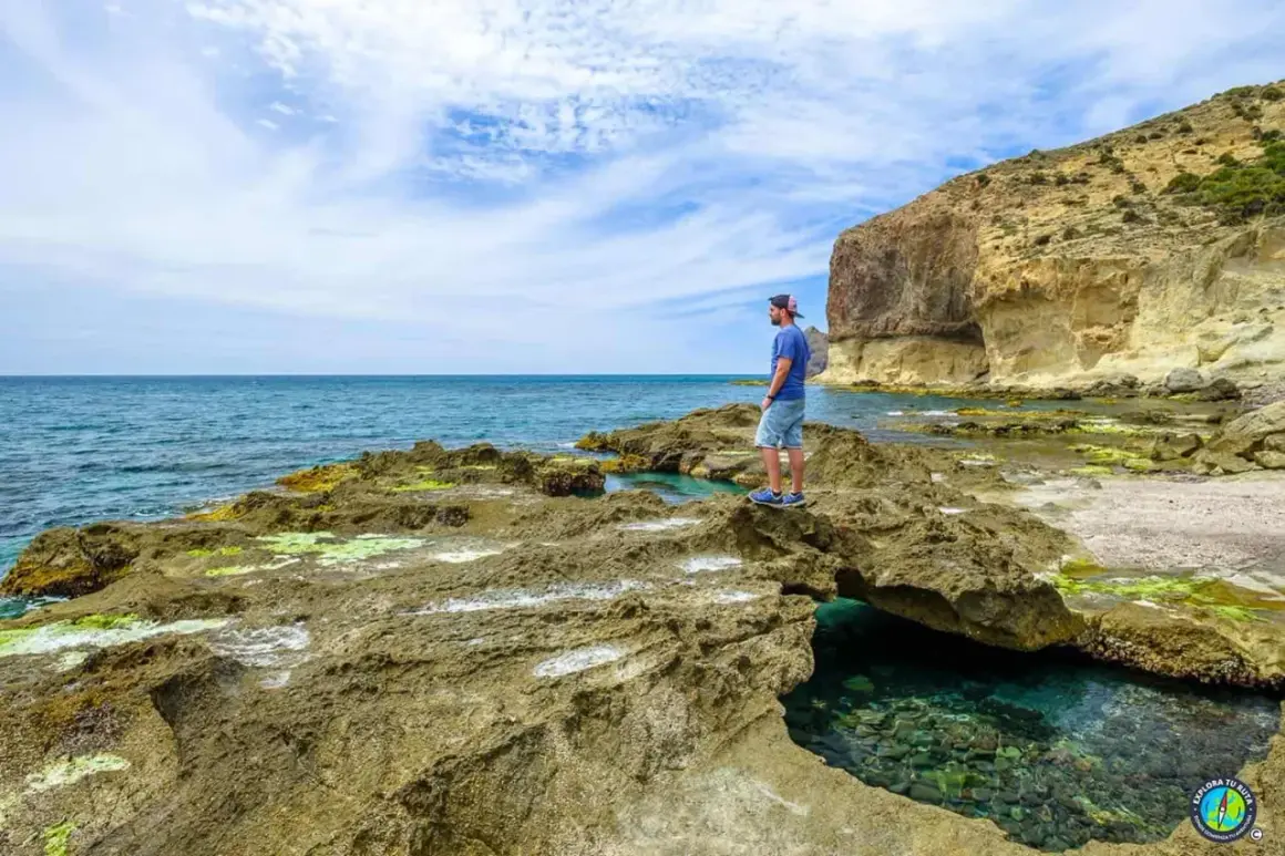 Hombre contempla el mar azul desde las rocas cerca del faro de Cabo de Gata. Acantilados y aguas cristalinas.