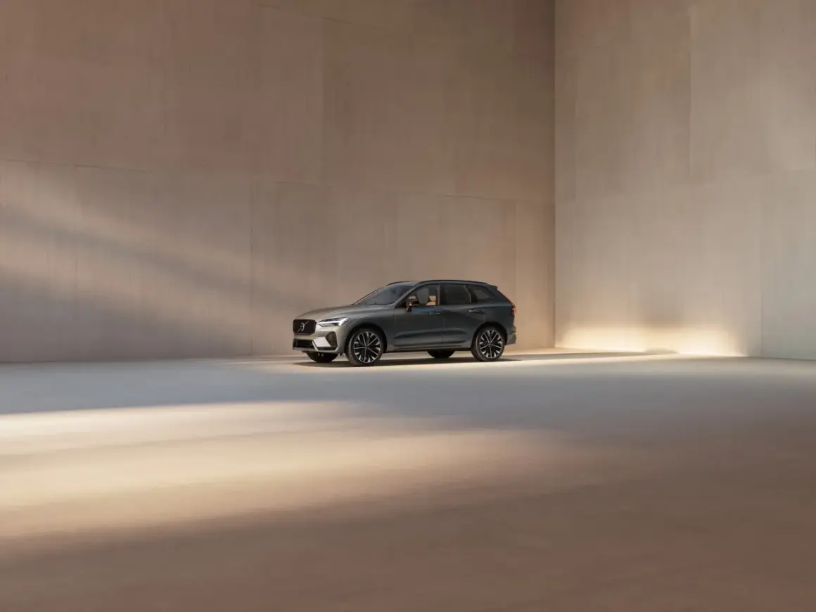 En mörkgrå Volvo XC60 står i ett ljust, minimalistiskt rum. Bilen visar upp sina eleganta linjer och fälgar, en perfekt representation av Volvo utrustningsnivåer.