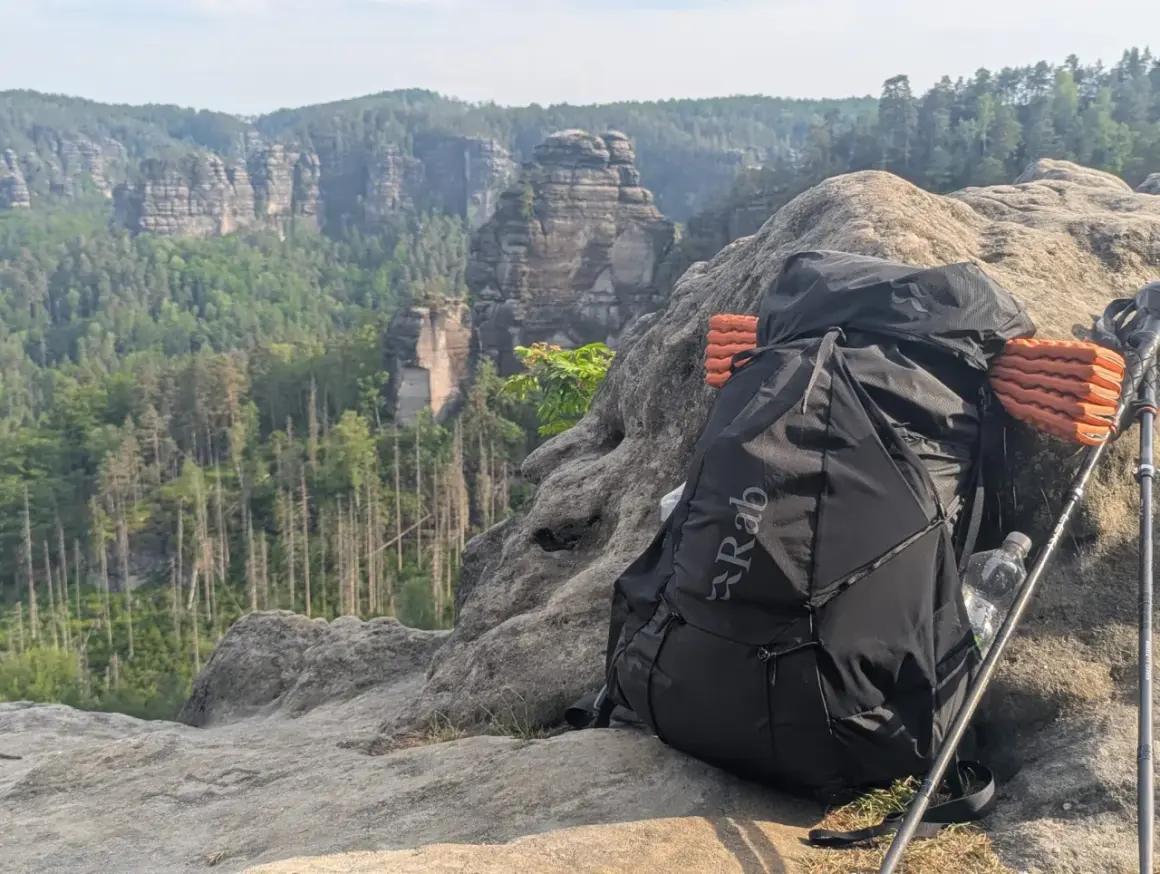 Rucksack und Wanderstöcke auf Felsen mit Bergpanorama. Alles pvc frei für umweltbewusstes Trekking.