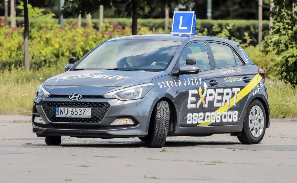 Szara Skoda z literą L na dachu, oznakowana jako "Szkoła Jazdy EXPERT". Pytanie o prawo jazdy od ilu lat jest tu na miejscu, bo to auto do nauki jazdy.