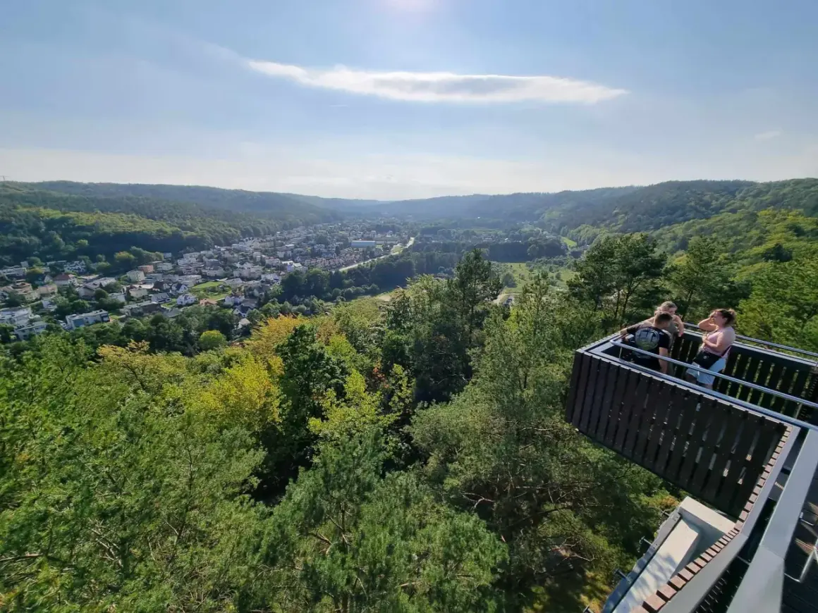 Widok z punktu widokowego w Rumi na zieloną dolinę i miasto. Kilka osób podziwia panoramę.