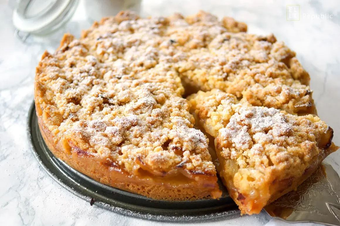 Saftiger apfelkuchen mit streusel, bestäubt mit Puderzucker. Ein Stück wurde bereits herausgenommen.