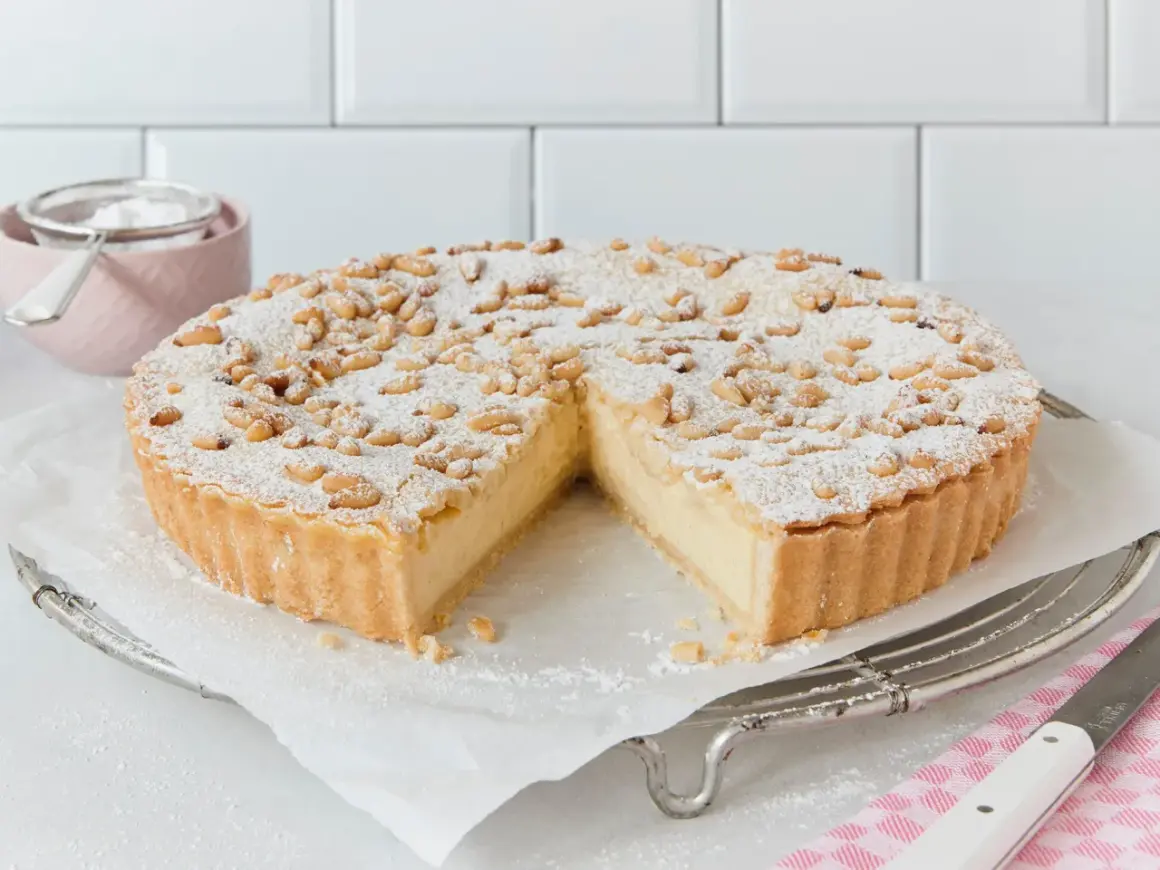 Eine köstliche Torta della Nonna, bestäubt mit Puderzucker und Pinienkernen, wartet darauf, angeschnitten zu werden.
