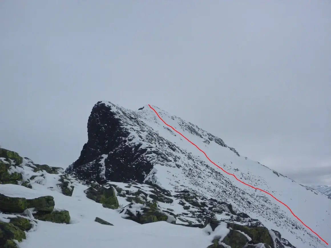 Snöklädda bergstoppar med en röd markerad led som leder uppåt. En utmanande sylarna topptur i vinterlandskap.
