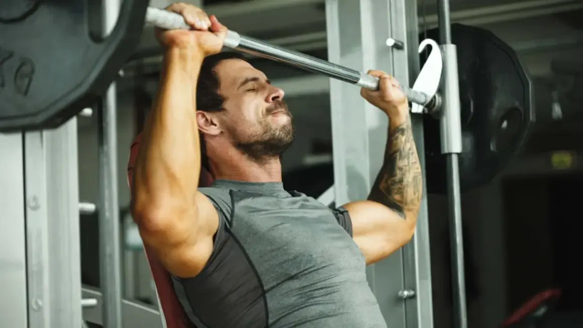 Mann hebt mit konzentriertem Gesichtsausdruck eine Langhantel im Fitnessstudio, ein intensiver 1 satz training.