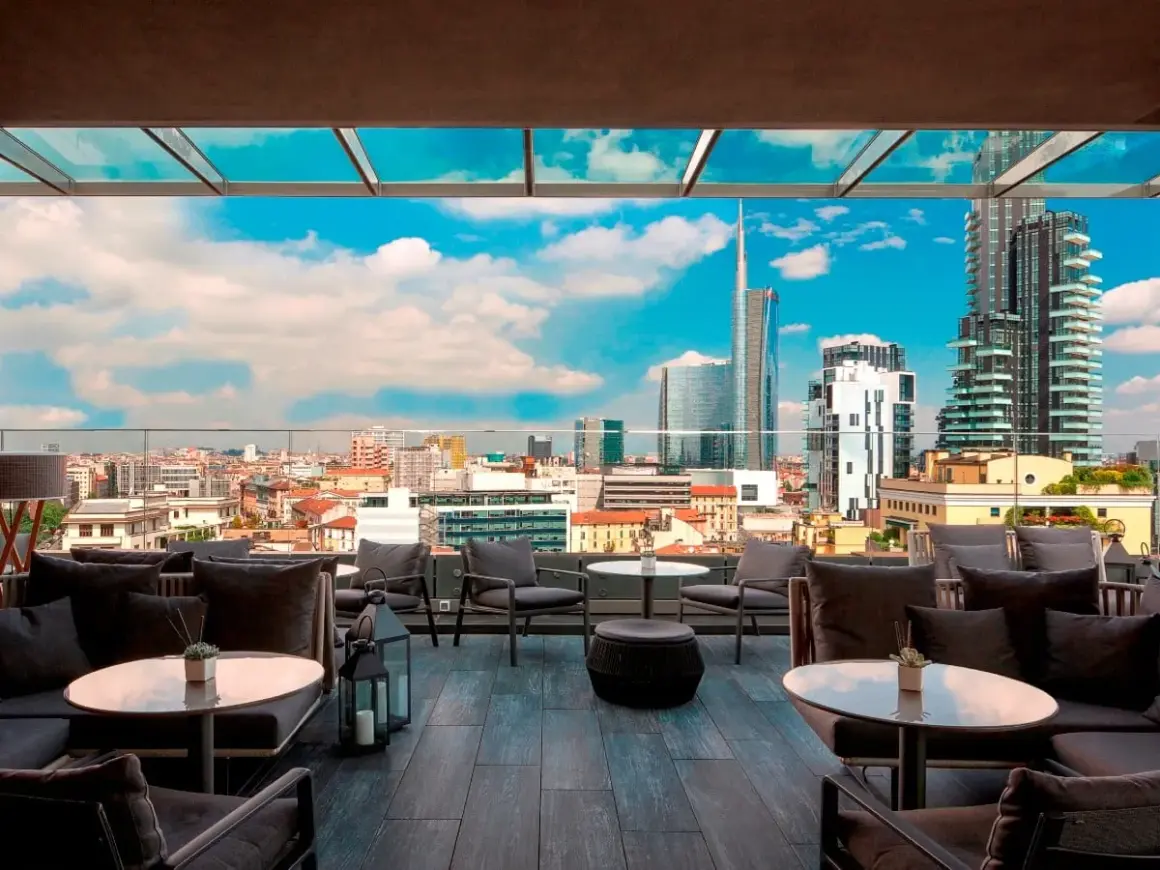 Terrazza panoramica con divani eleganti e vista sui grattacieli di Milano. Perfetto per godersi l'aperitivo nei locali chic milano.