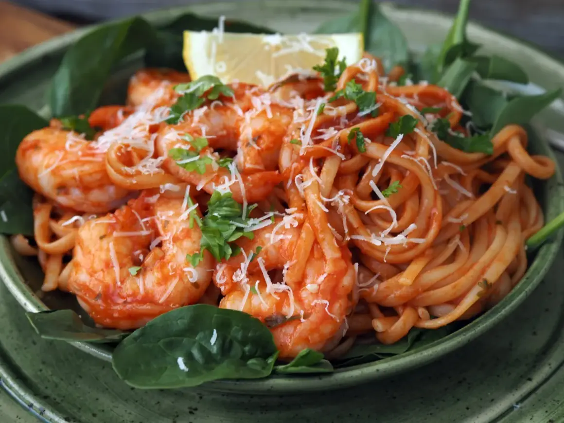 En skål med pasta pomodoro med räkor, toppad med riven ost och färsk persilja. En citronklyfta vilar ovanpå.
