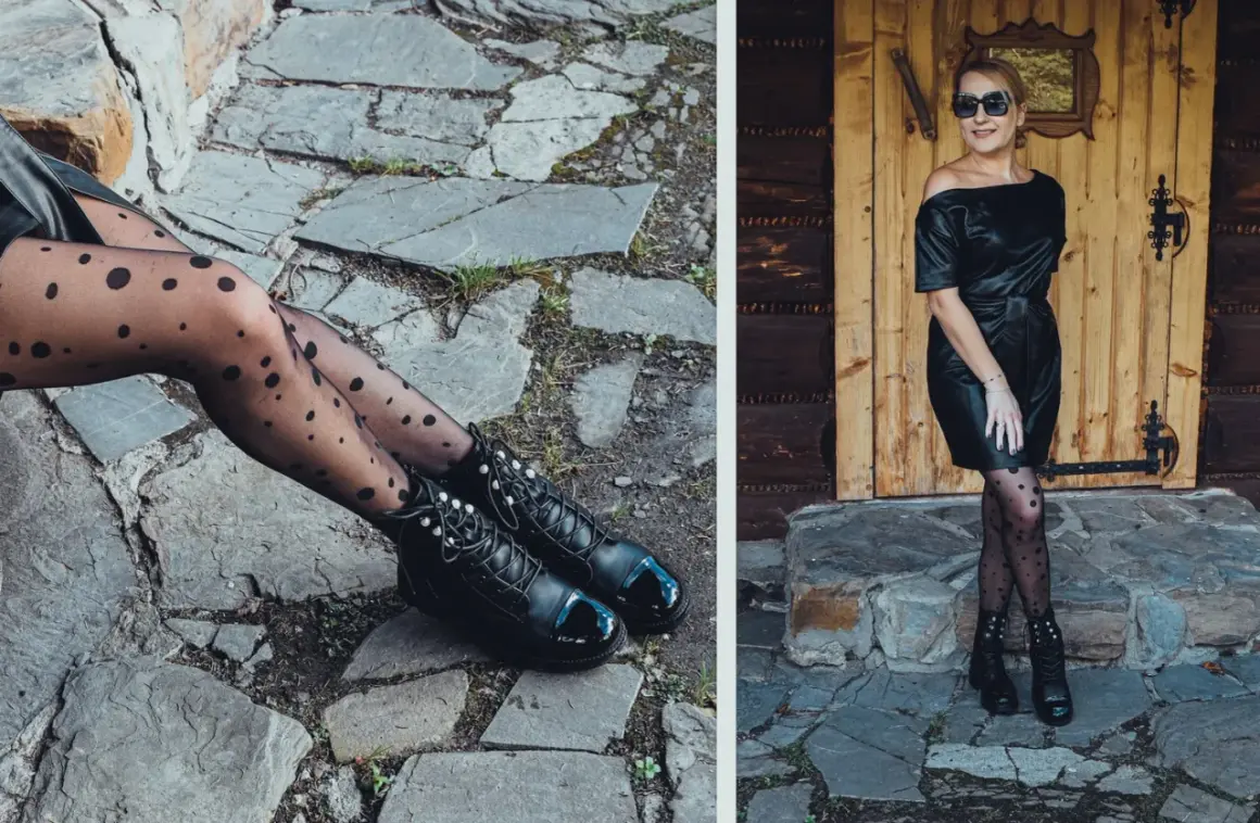 Elegancka kobieta w czarnej sukience z ekoskóry i rajstopach w kropki, pozuje na tle drewnianych drzwi.