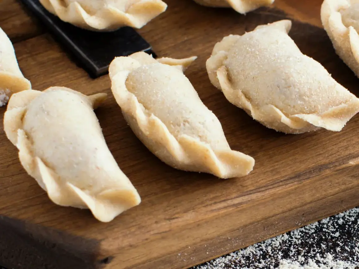 Surowe pierogi na desce. Zastanawiasz się, ile gotować pierogi, by były idealne?