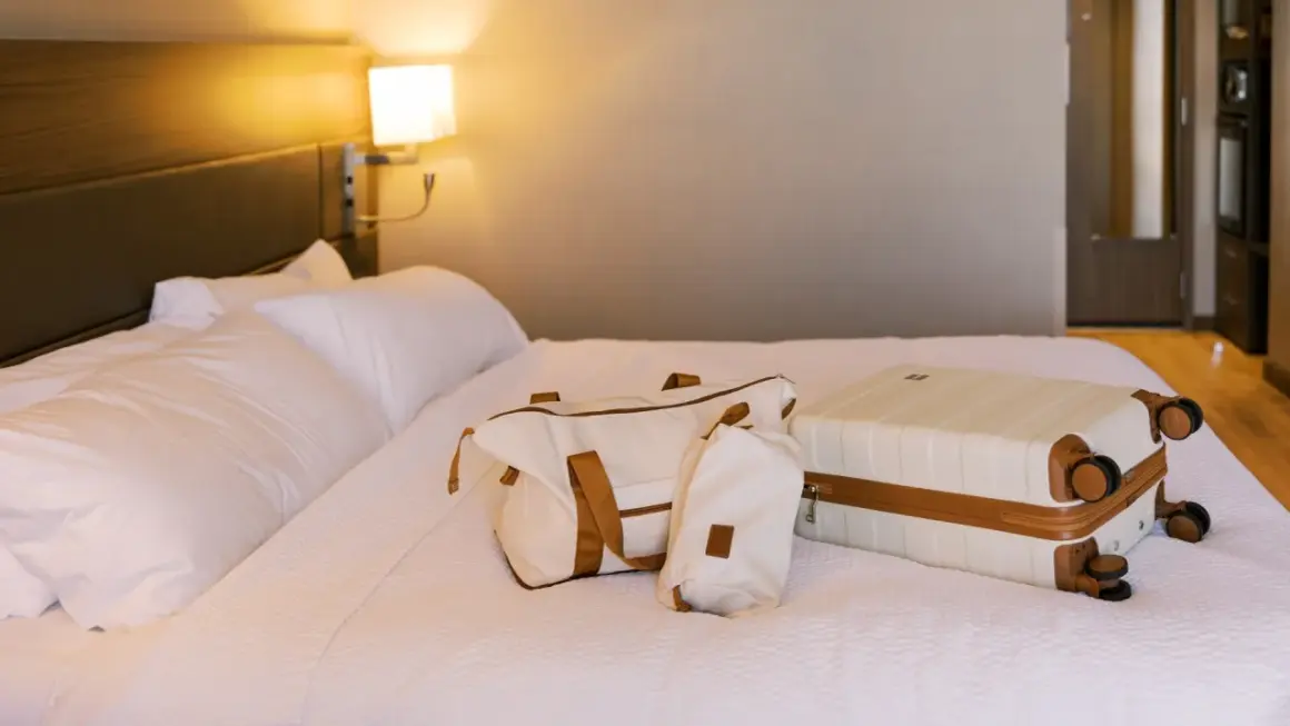 Biała walizka i torba podróżna na łóżku w hotelu.