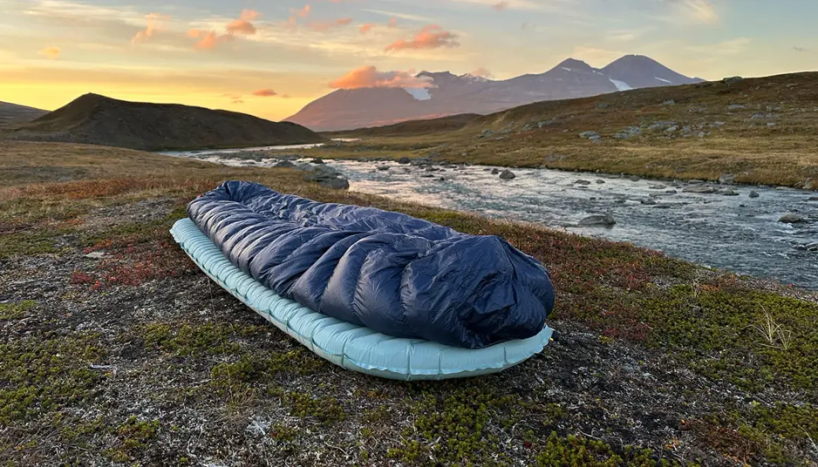 Sovsäck och liggunderlag redo för en natt i fjällen. Test av liggunderlag vid en forsande älv i solnedgången.