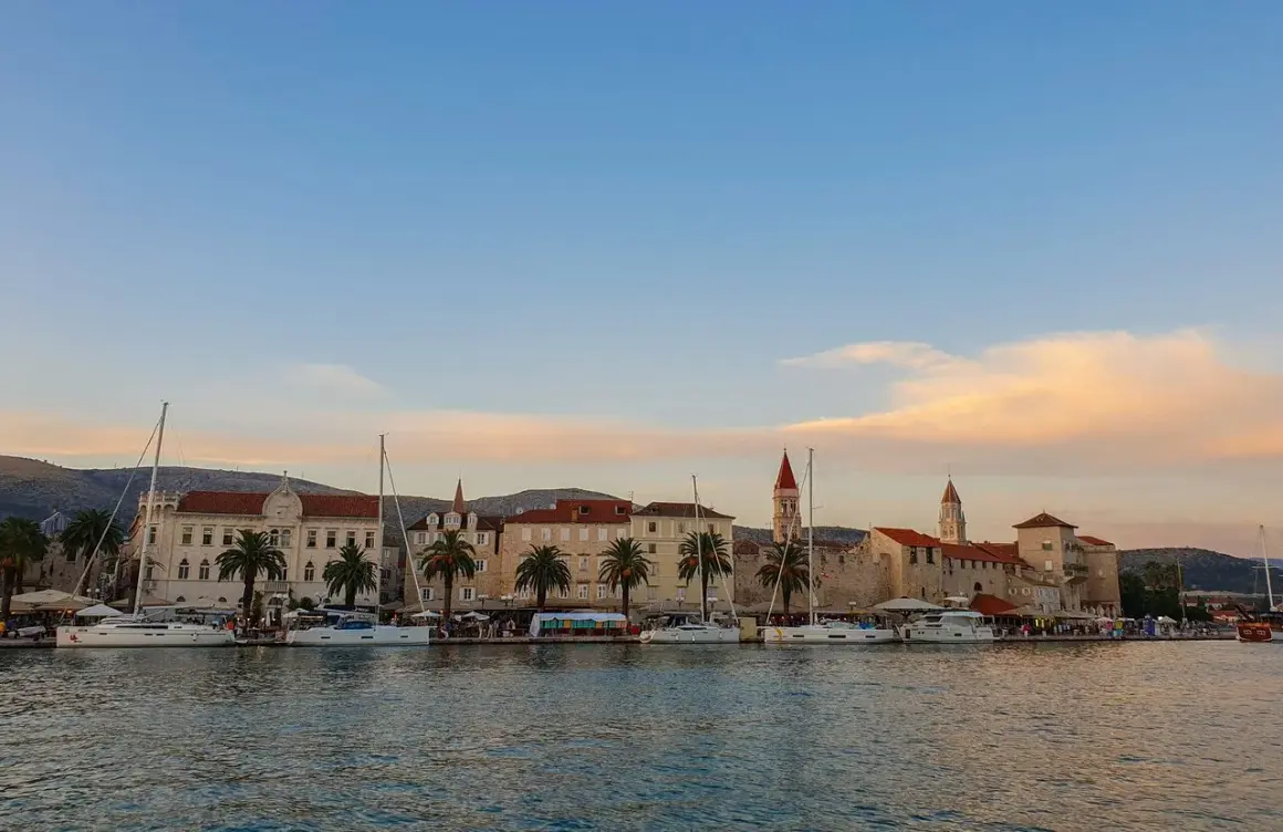 Trogir co zobaczyć: malownicza starówka z palmami i żaglówkami przy nabrzeżu, w blasku zachodzącego słońca.
