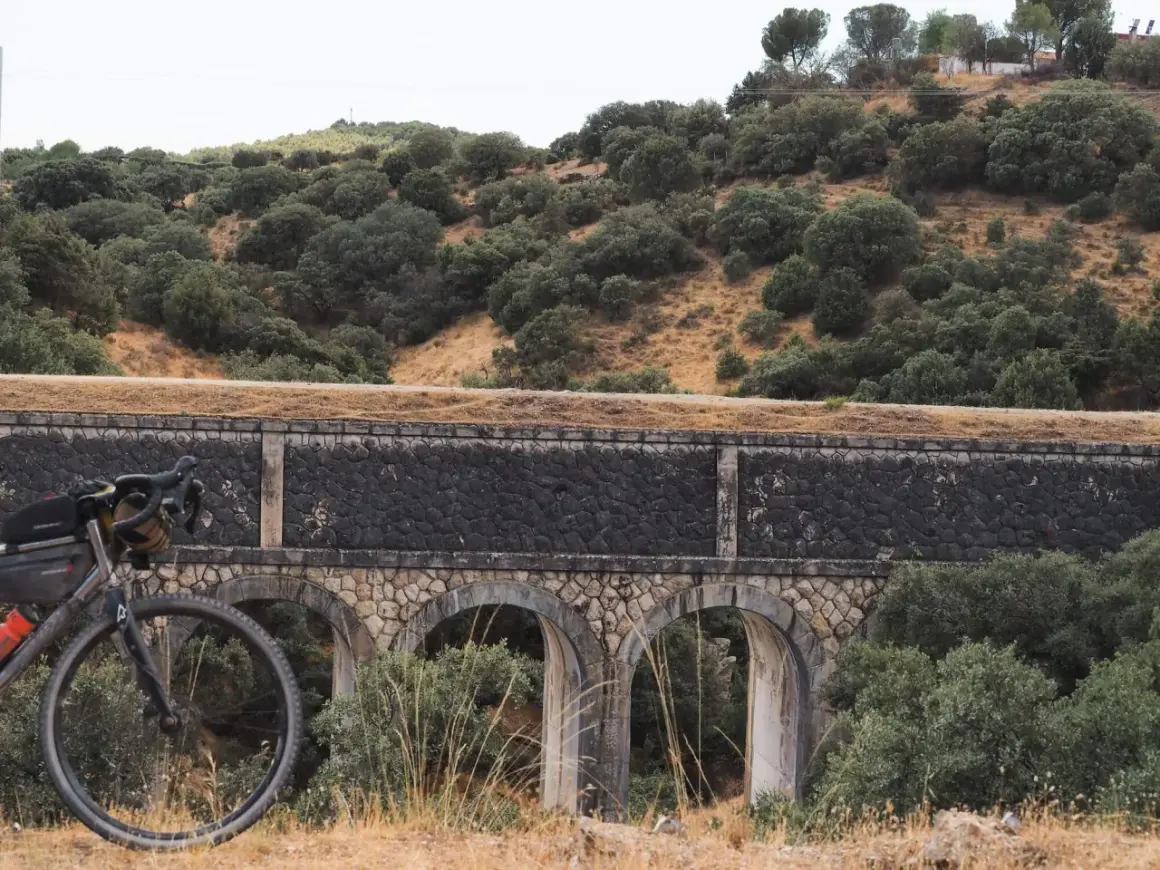 Bicicleta gravel lista para explorar las **rutas gravel Madrid** junto a un antiguo acueducto entre encinas.