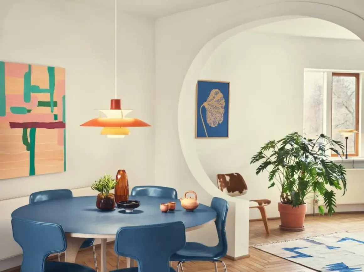 Ein Esszimmer im **mid century modern** Stil mit blauem Tisch, blauen Stühlen, einer bunten Wandkunst und einer markanten Hängeleuchte.