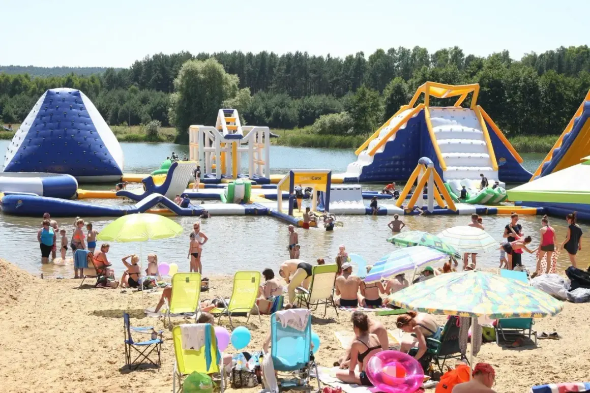 Ludzie bawią się na dmuchanych atrakcjach wodnych na **bolmin zalew**. Słoneczny dzień, plaża pełna wypoczywających.