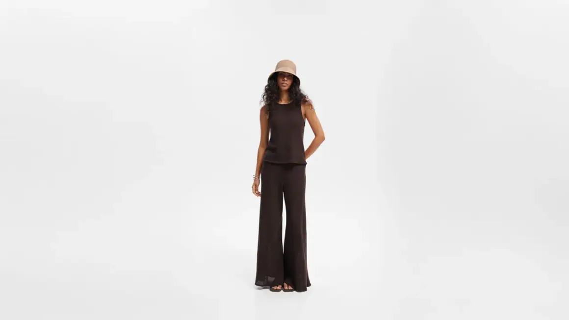 Modelka w brązowym topie i czarnych szerokich spodniach, uzupełniona kapeluszem typu bucket hat. Stylowe czarne szerokie spodnie stylizacje.