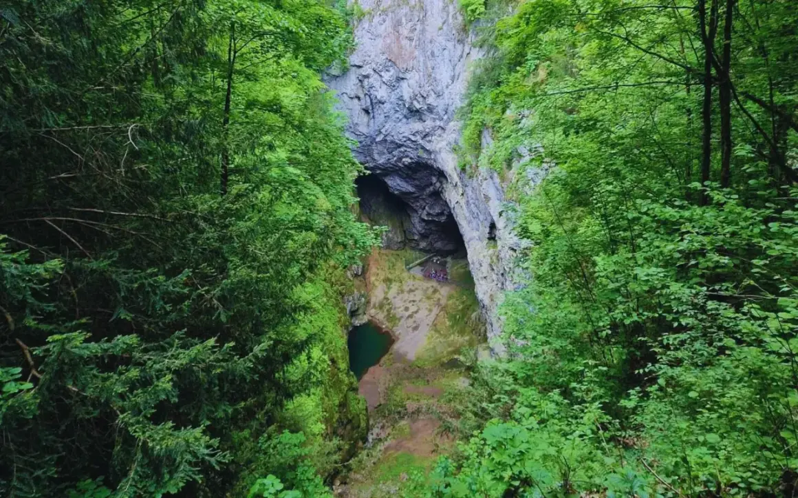 Jaskinia Macochy: jak dojechać do tego cudu natury? Widok z góry na wejście do jaskini, zielony staw i skalne ściany.