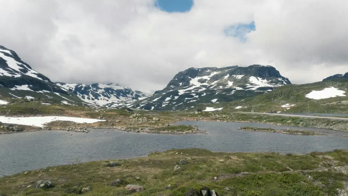 Vacker vy över Hardangervidda med snöklädda berg, en sjö och en väg. Perfekt för en vandring.