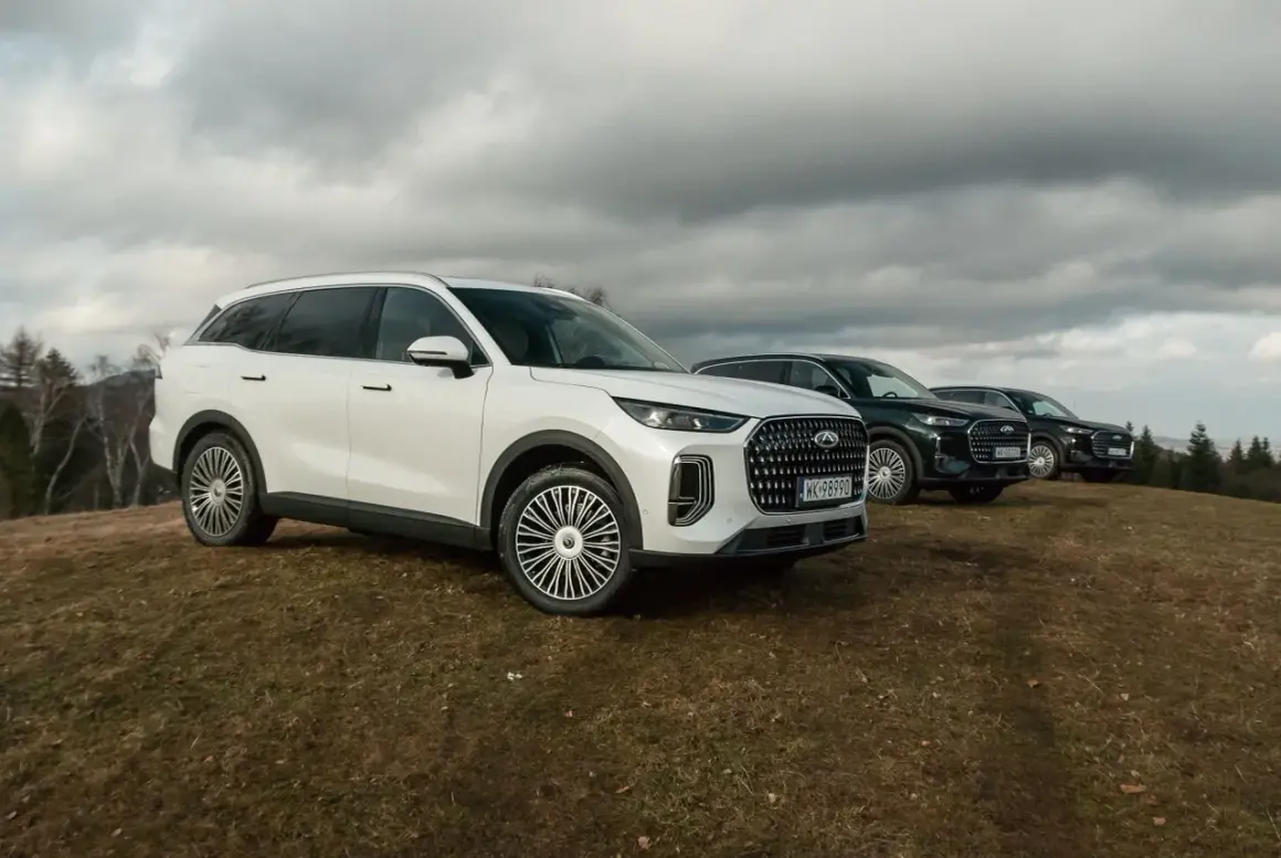 Biały Jaecoo 9 i dwa ciemne SUV-y na wzgórzu pod pochmurnym niebem.