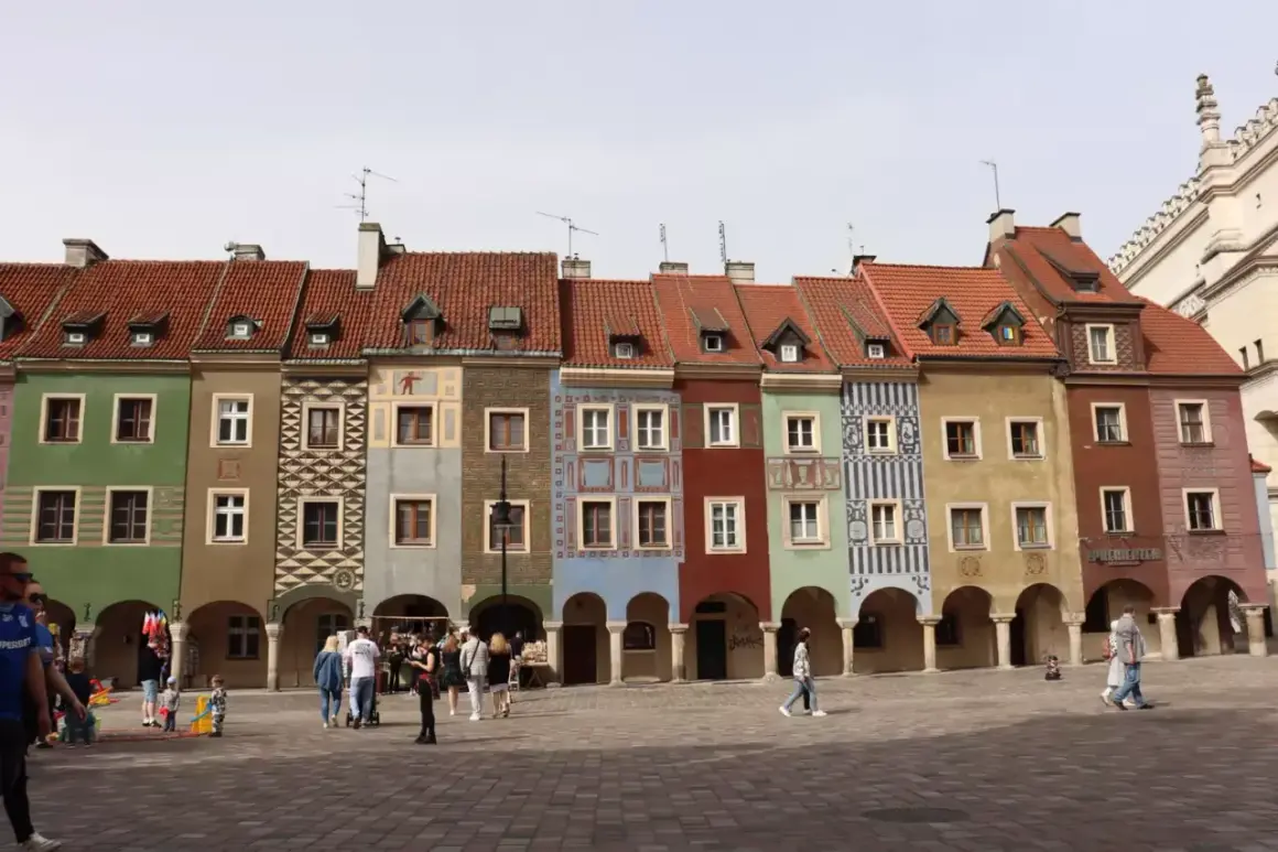 Kolorowe kamieniczki na poznańskim rynku, z arkadami i ludźmi spacerującymi po bruku.