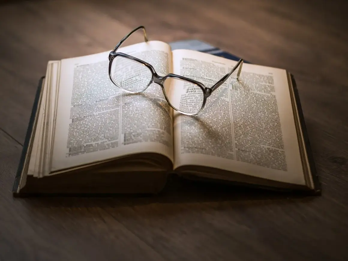 Eine Brille liegt auf einem aufgeschlagenen Buch mit informierenden Texten.