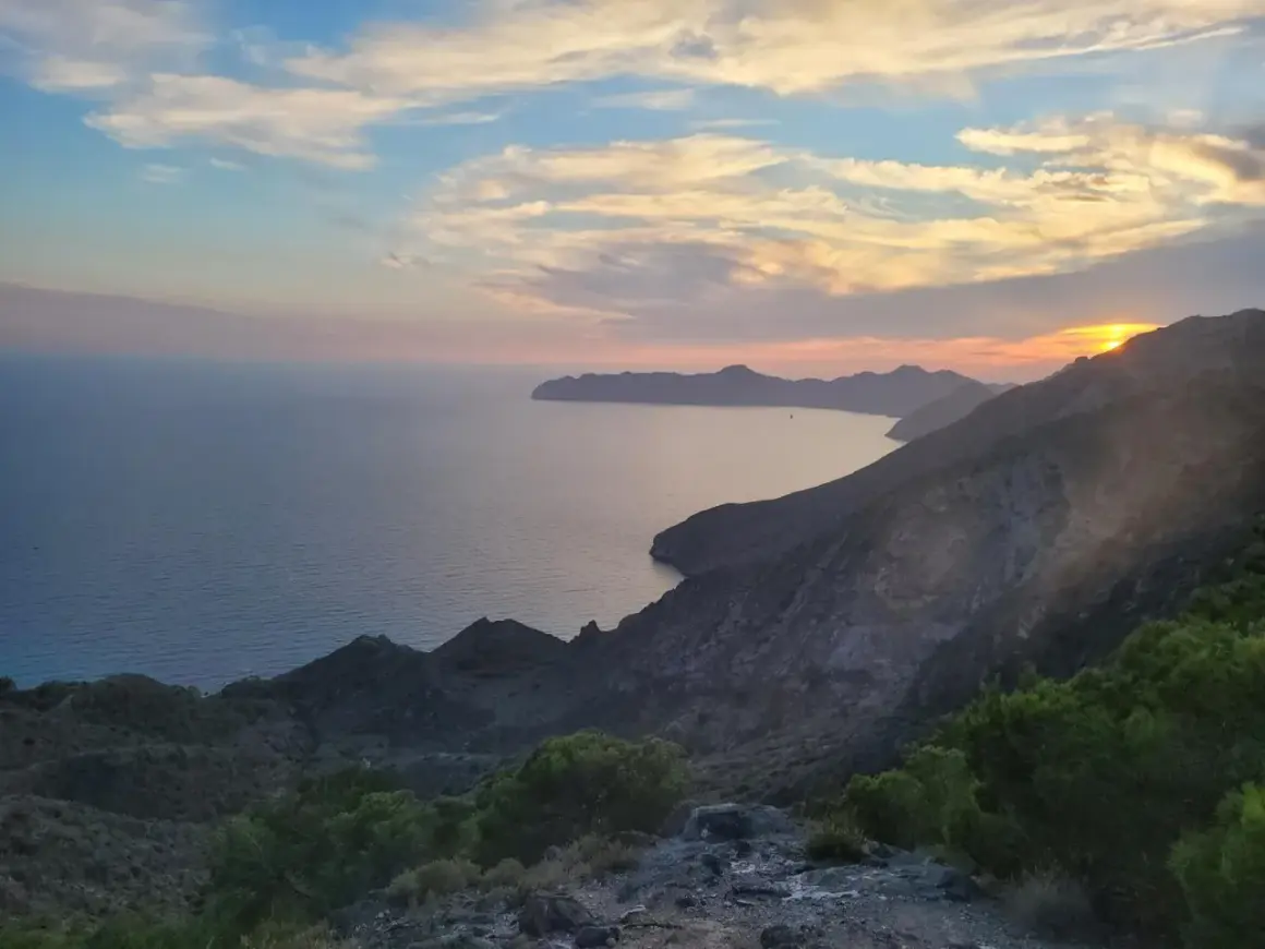 Atardecer en el mirador del Roldán, con el mar Mediterráneo y montañas escarpadas bajo un cielo de nubes rosadas y anaranjadas.