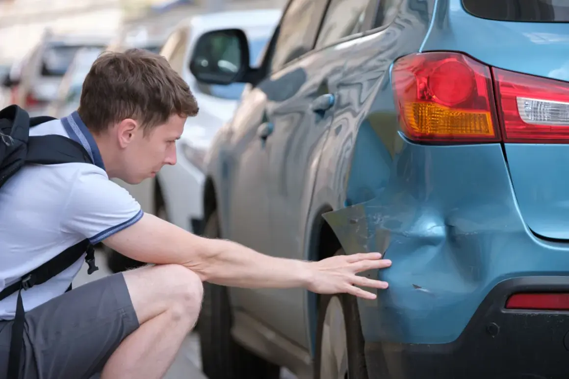 Mann untersucht Delle am blauen Auto. Hoffentlich keine Geisterfahrer-Strafe wegen des Schadens.