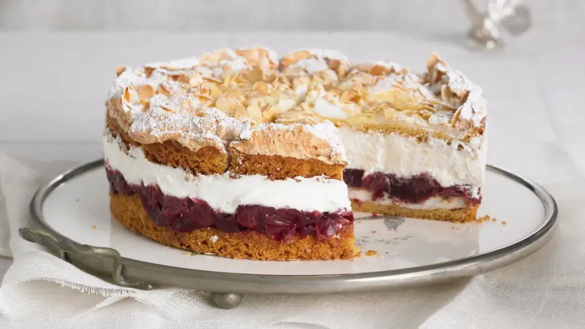 Eine köstliche Hansen Jensen Torte mit Kirschen, Sahne und Baiserhaube, bestreut mit Mandelblättchen und Puderzucker.