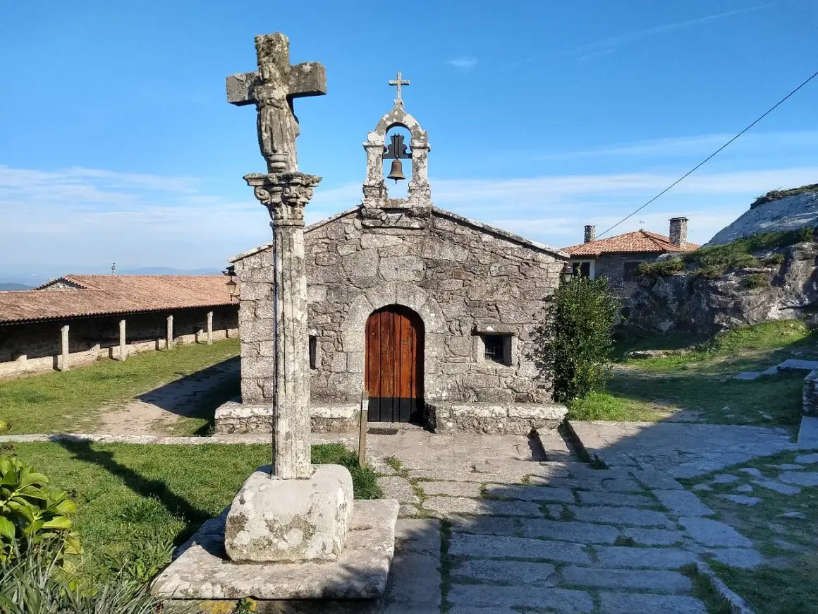 Crucero y ermita de piedra en el Castro de Santa Trega, bajo un cielo azul.
