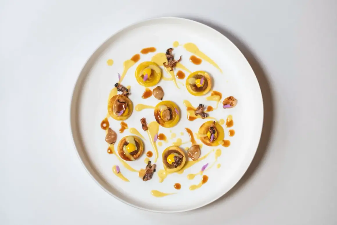 Piccolo capolavoro culinario: tartellette dorate con ripieno giallo, guarnite con calamari croccanti e fiori viola. Un'opera d'arte degna di un ristorante con massimo stelle Michelin.