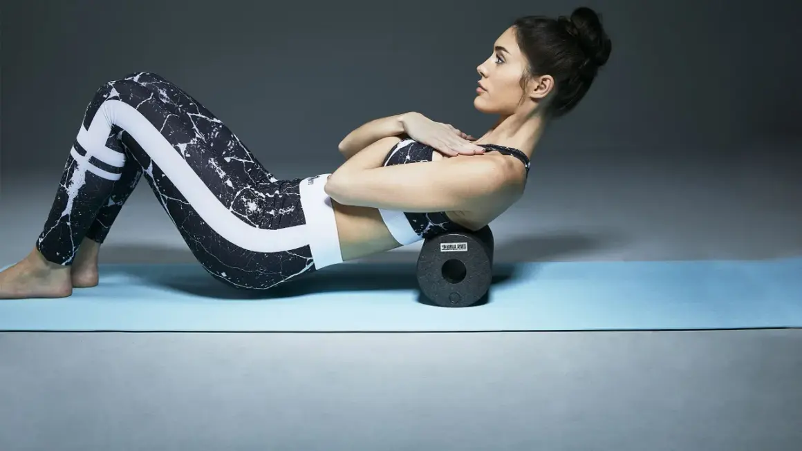 Kvinnan på yogamattan använder en foam roller för att stretcha ryggen, ett steg mot att få magrutor.
