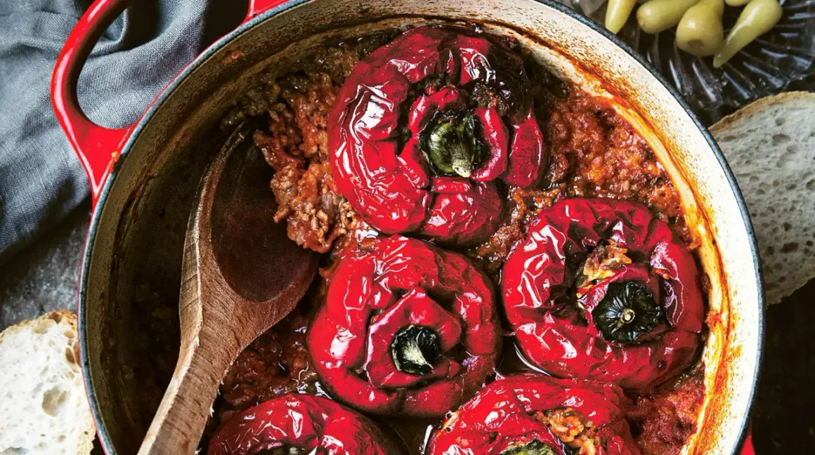 Röda, fyllda paprikor i en gryta med köttfärs och ris, redo att serveras med en träsked och en bit bröd.