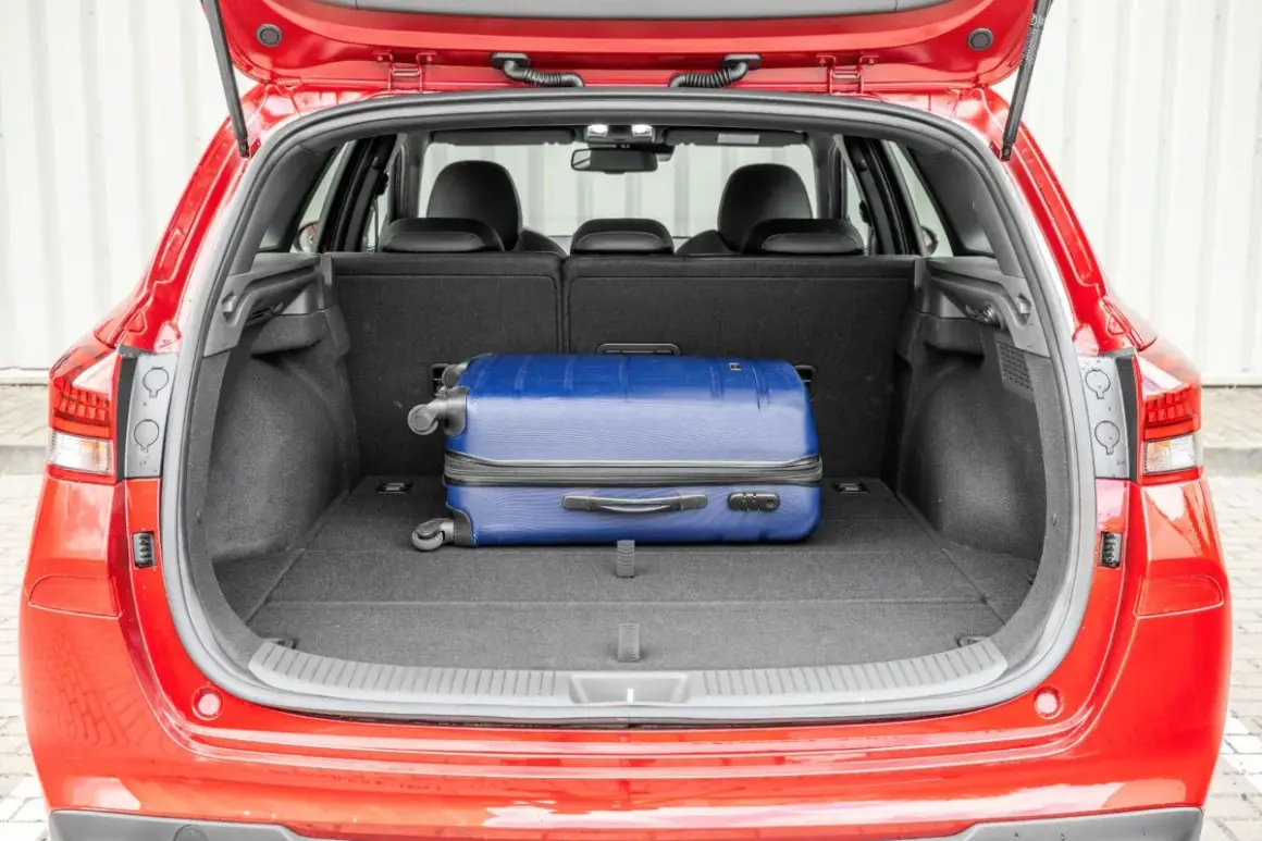 Otwarty bagażnik czerwonego Hyundai i30 kombi z niebieską walizką. Sprawdź pojemność bagażnika na podróż!