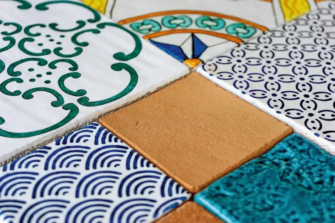 Composizione di mattonelle fai da te con decori geometrici e floreali in blu, verde e giallo, alternate a tasselli color sabbia e turchese.
