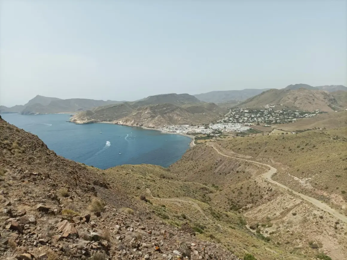 Vista panorámica de la costa de Almería, con el mar azul, un pueblo blanco y el paisaje árido del cerro negro.