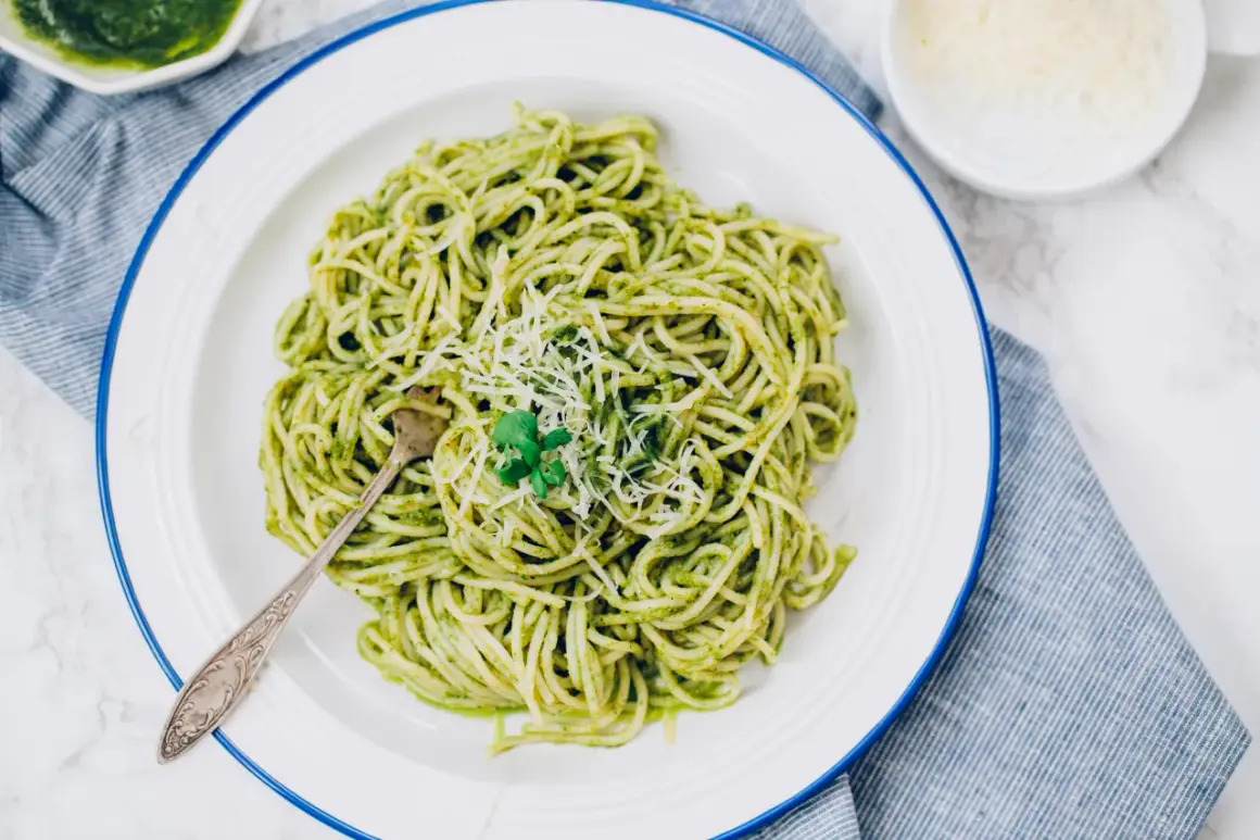 Porcja spaghetti z zielonym pesto, posypana parmezanem, na białym talerzu.