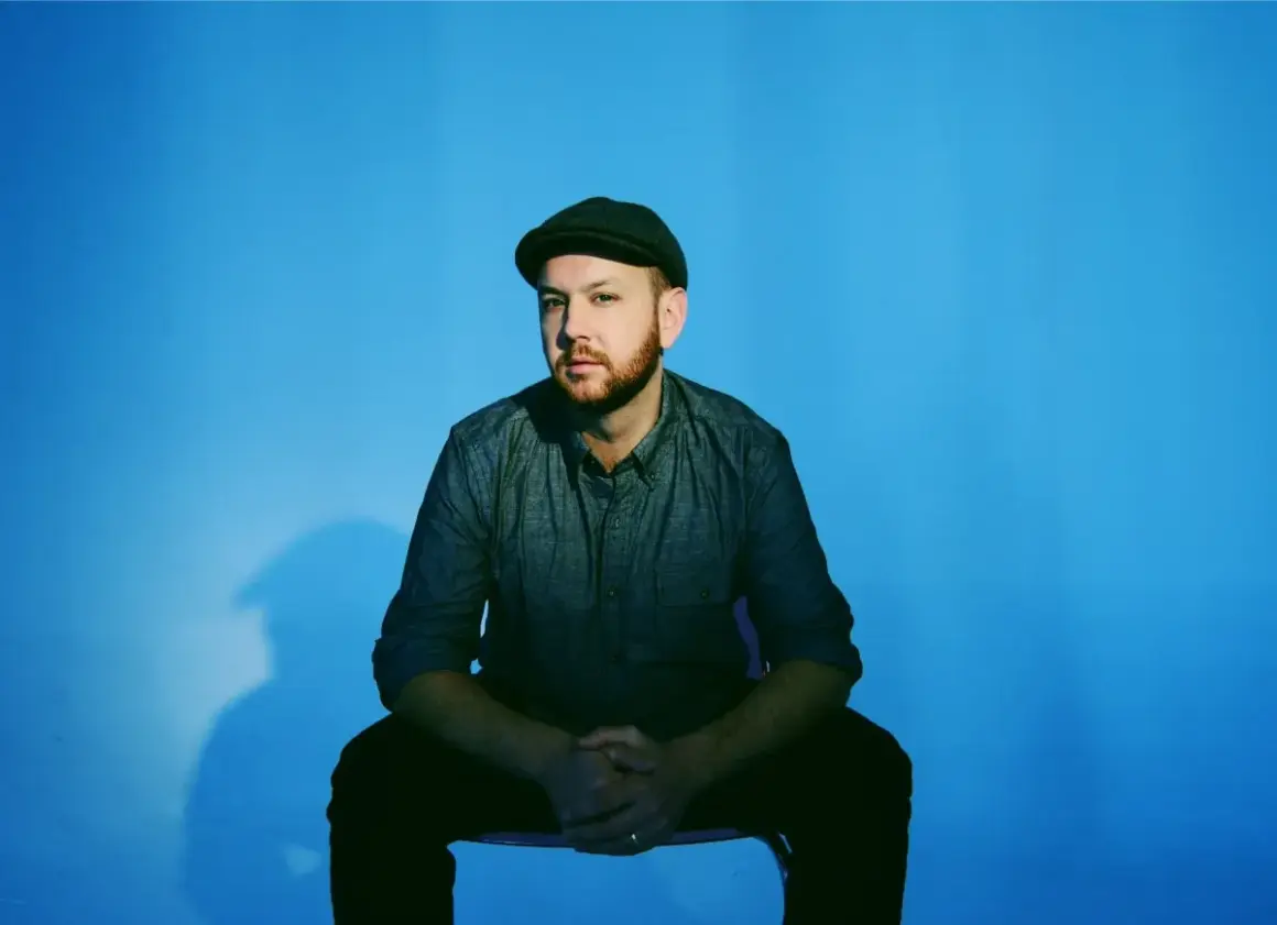 Matt Simons, nach dem Erdrutsch, sitzt nachdenklich vor blauem Hintergrund.