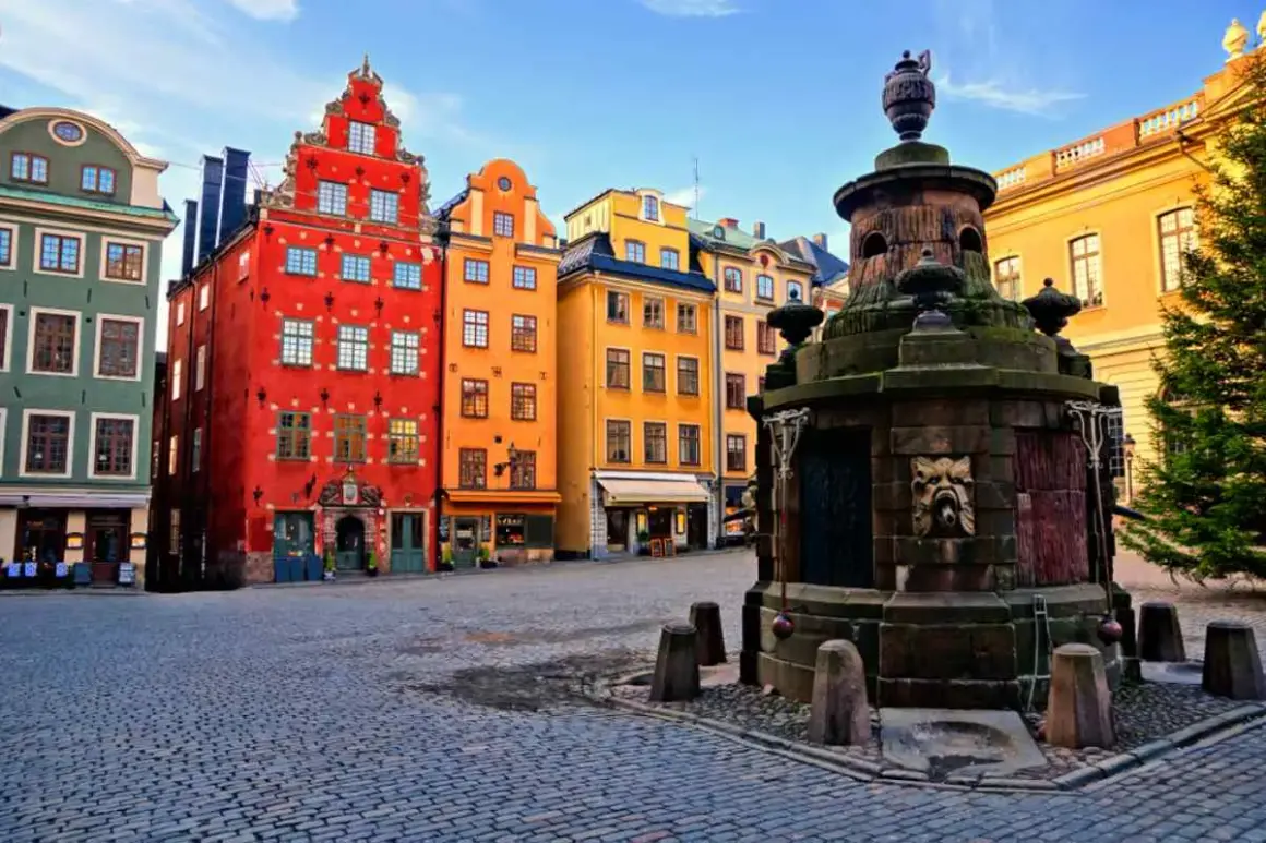Färgglada hus i Gamla Stan, Stockholm, med en gammal fontän på kullerstensbelagd plats.