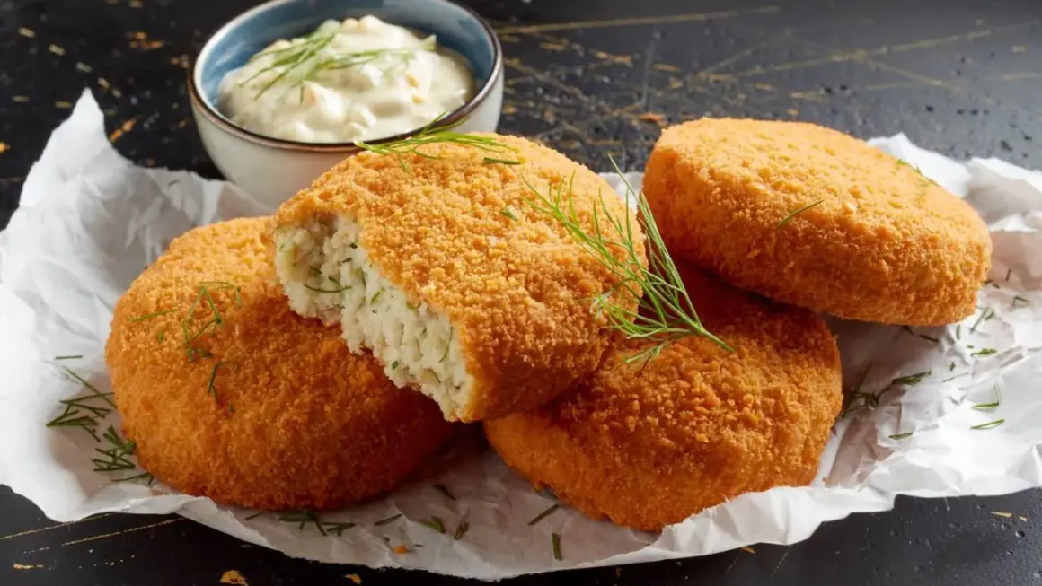 Crujientes croquetas de merluza doradas, una partida revela su interior tierno. Servidas con una cremosa salsa y eneldo fresco.