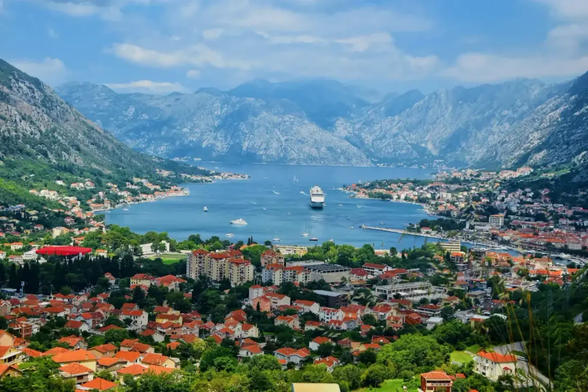 Vacker vy över Kotorbukten i Montenegro. Ett kryssningsfartyg ligger för ankar i det blå vattnet, omgivet av berg och en stad med röda tak. Montenegro mat kan avnjutas med en sådan här utsikt.