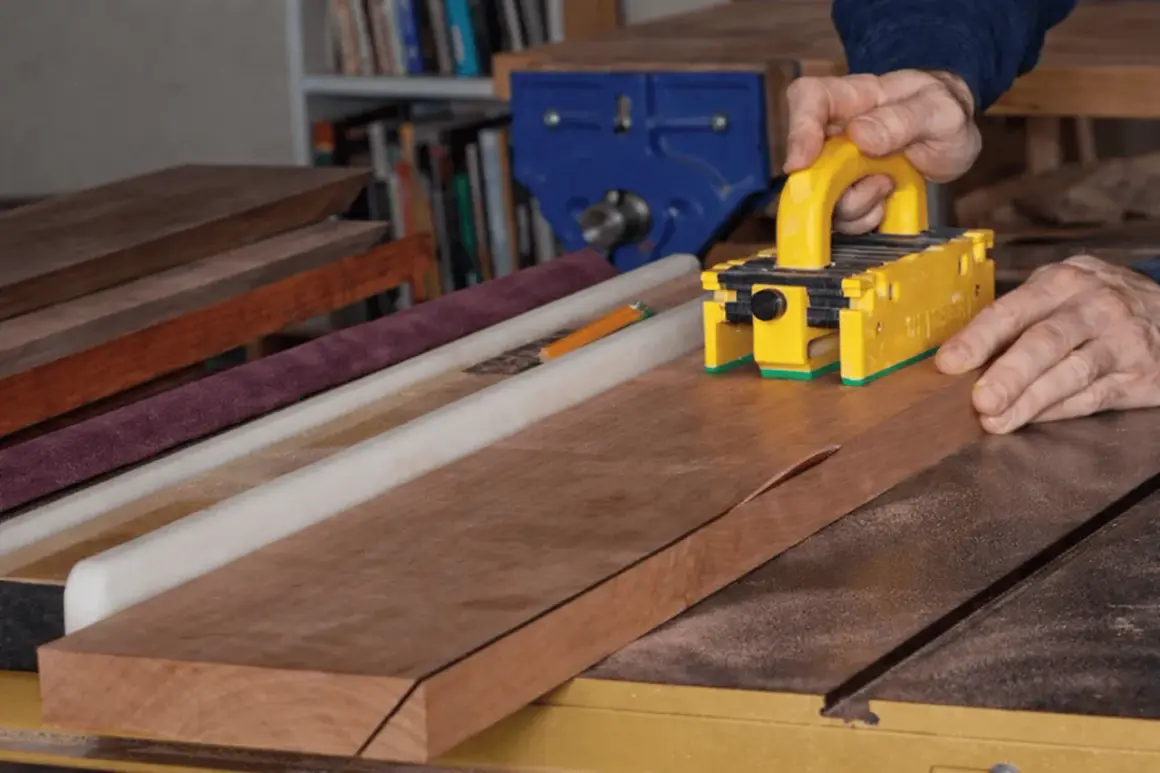 Maintenant, je vais fabriquer une scie sur table. Un artisan utilise un poussoir jaune pour guider une planche de bois sur la scie.